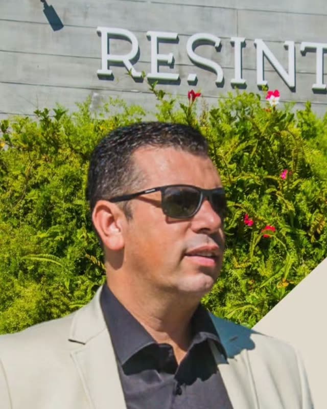 Adriano de blazer bege e óculos escuros em frente ao Re.sinto